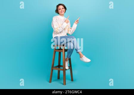 Full body length cadre of optimistic girl indicating fingers empty space price list sitting cafe chair isolated on blue color background Stock Photo