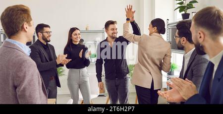 Two young men doing high five while their cheerful coworkers applauding them Stock Photo
