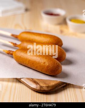 Deep fried corn dogs on parchment paper with ketchup and mustard in the background with napkins Stock Photo