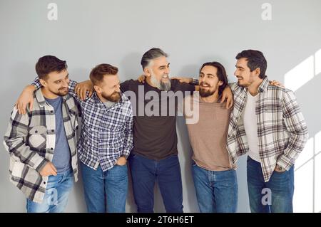 Male bearded friends looking cheerful to each other and smiling on grey wall background. Stock Photo