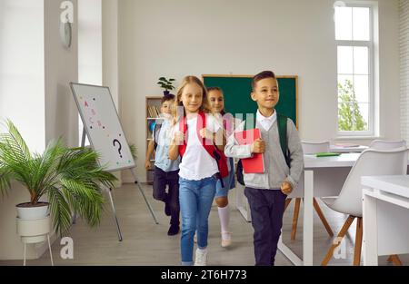 Funny elementary school students walking out of classroom together after lesson. Stock Photo