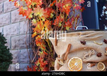 Mulled wine pan decorated with cinnamon, star anise and dried oranges on background of stone wall with autumn leaves Stock Photo