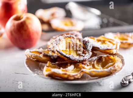 Mini tarts made of puff pastry and sliced apples sprinkled with powdered sugar on white plate. France apple cakes - Close up. Stock Photo