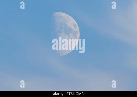 A partial moon sphere with visible craters moves across the blue sky after sunset. Stock Photo