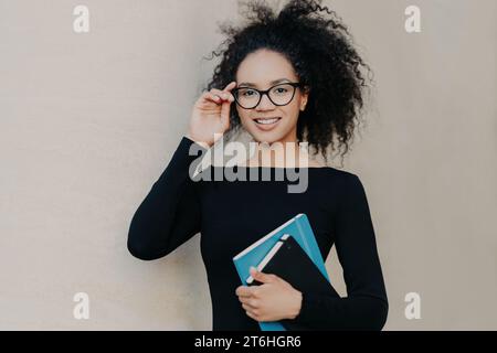 Smart young professional adjusting glasses, holding a tablet, with a friendly smile Stock Photo