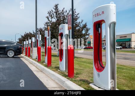 BEMIDJI, MN – 3 JUN 2023: A row of Tesla Supercharger Charging Stations near the street with a black EV car plugged in for recharging. Stock Photo