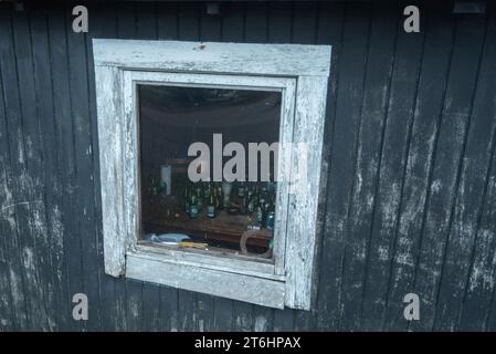 Beer bottles and cigarette packets behind the window of an old fishing hut, Klintholm Havn, Mön, Denmark Stock Photo