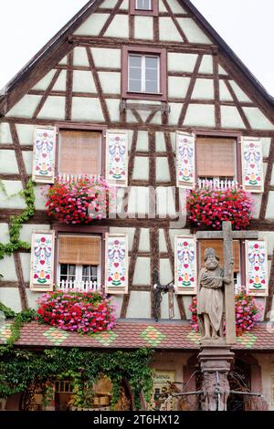 The half-timbered house 'Loewert' from the 16th century with colorfully painted shutters and the Konstatin fountain in Kaysersberg, Alsace Stock Photo