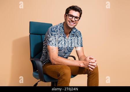 Photo of young cheerful team leader sitting boss armchair waiting for interview with new candidates isolated on beige color background Stock Photo