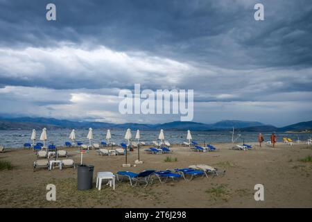 Kalamaki, Corfu, Greece, sun beds and umbrellas at Kalamaki beach in the northeast of the Greek island of Corfu, in the background the mainland of Albania with the seaside resort of Saranda. In front forgotten children's toys, bucket and shovel. Price board umbrella and sun lounger rental. Stock Photo