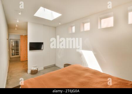 a bedroom with an orange comforter on the bed and a flat screen tv mounted in the corner of the room Stock Photo