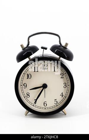 A black alarm clock featuring two bells on top, chrome handle, and legs, captured against a pristine white background. The design blends classic elega Stock Photo