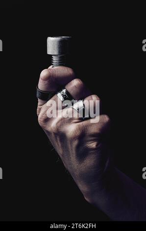 Big male hand with rings holding big stainless steel bolt Stock Photo