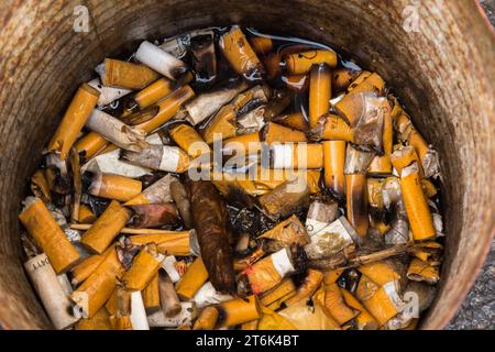 Discarded wet cigarette butts in metal can ashtray. Stock Photo