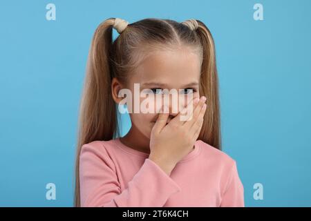Embarrassed little girl covering her mouth with hand on light blue background Stock Photo