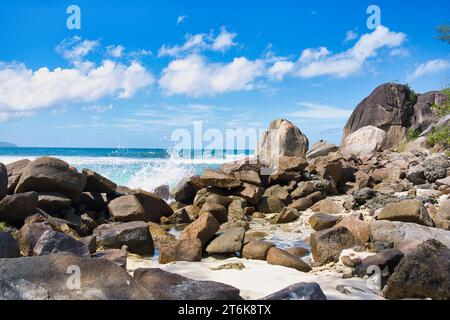 Sunny, white sandy beach, docked fishing boat, huge granite rocks between tree trunk at Baie Lazare beach, Mahe, Seychelles Stock Photo