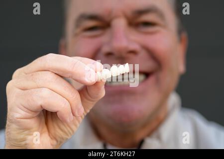 Extreme close up of a man holding his Dental prosthesis with his fingers, focus on hand Stock Photo