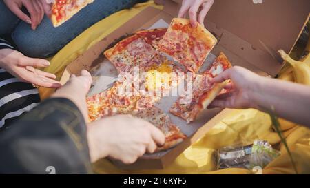 Young students' hands reach for the pizza. Stock Photo