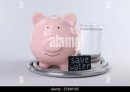 Water scarcity concept. Card with phrase Save Water, piggy bank, shower hose and glass of drink isolated on white Stock Photo