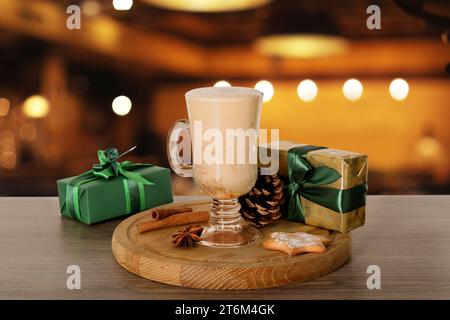 Glass of delicious eggnog, spices, cookie and gift boxes on wooden table in bar Stock Photo