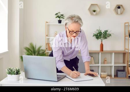 Beautiful senior businesswoman writing down information in notebook or signing documents. Stock Photo