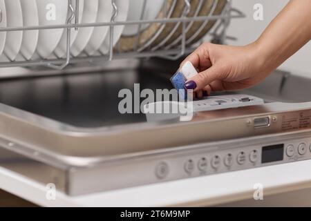 female hand puts dishwasher tablet into open automatic built-in dishwasher machine with dirty dish inside in kitchen Stock Photo