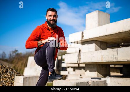 Adult man is exercising outdoor on sunny day. He is stretching his body. Stock Photo