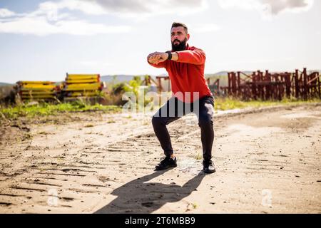 Young man is exercising outdoor. He is doing squats. Stock Photo