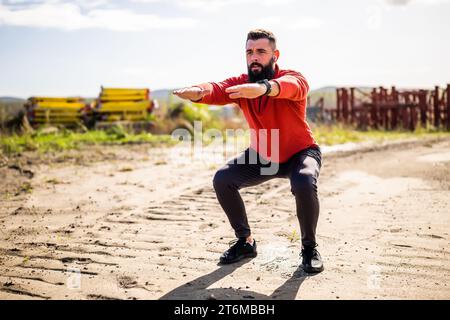 Young man is exercising outdoor. He is doing squats. Stock Photo