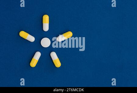Summer yellow sun from pills tablets on blue surface with copy space. Minimalistic medicine concept. Stock Photo