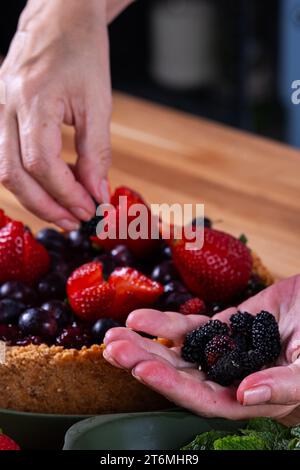 female hands decorating a berry pie with fruits. Stock Photo