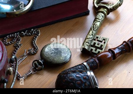 Vintage still life. Old pocket watch, antique key, smoking pipe and book with magnifier on wooden background. Stock Photo