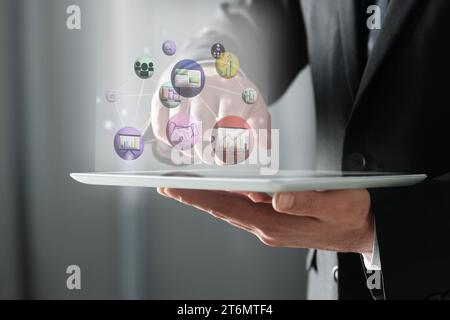 Marketing strategy. Man using tablet computer on grey blurred background, closeup. Virtual screen with icons over device Stock Photo
