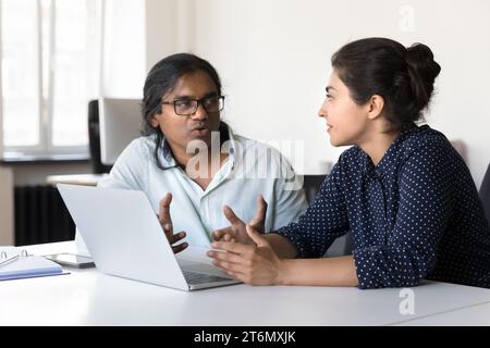 Two serious Indian diverse employees talking at laptop Stock Photo