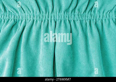Turquoise corduroy fabric gathered with elastic close-up. Velveteen texture with folds and drapery. Cloth surface, textile background, wallpaper, back Stock Photo
