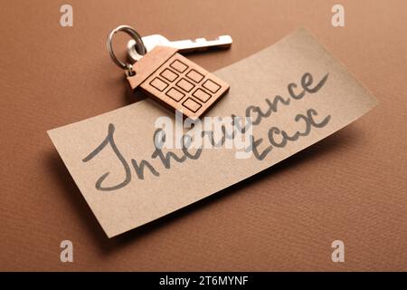 Card with phrase Inheritance Tax and key with house shaped key chain on brown background, closeup Stock Photo