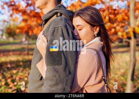 Close up of woman hugging husband in ukrainian military uniform with flag chevron from back. Sad stressed loving couple Stock Photo