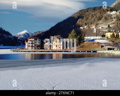 Alleghe church and houses in front of a partially frozen lake. Stock Photo