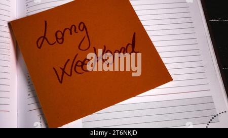 Writing long weekend on memo post reminder. Text long weekend on sticky paper. Stock Photo