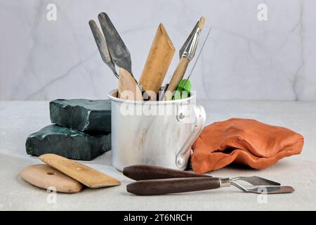 Tools for modeling from plasticine and clay in a metal mug and pieces of clay and plasticine on a white concrete table in a sculpture workshop Stock Photo