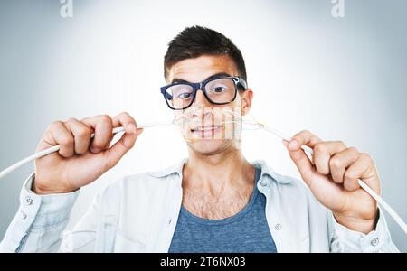IT support, cable and power with an electrician man in studio on a gray background for troubleshooting. Face, hands and glasses with an engineering Stock Photo