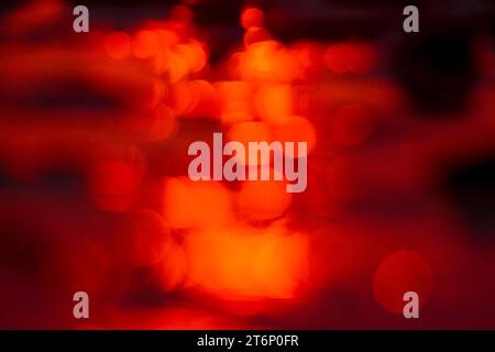 Red out of focus specular highlights created by a setting sun reflecting off moving water Stock Photo