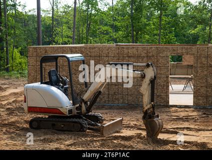 Mini excavator parked on the dirt outside a new home building project at a construction site. Stock Photo