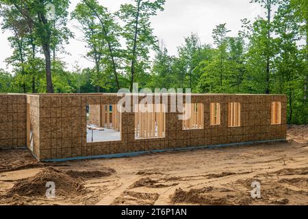 New home building site in early construction stage, with plywood on exterior walls with window openings and wood framing studs inside, on a wooded lot Stock Photo