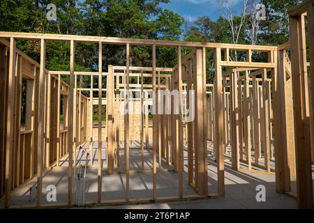 Closeup of wood framing studs of interior walls at new home construction work site in sunshine with shadows, with trees in the background. Stock Photo