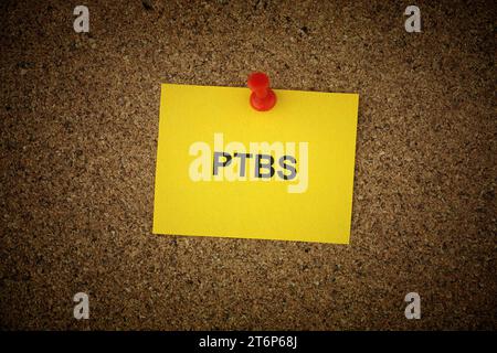 A yellow paper note with the abbreviation PTBS - Posttraumatic stress disorder (in German) on it pinned to a cork board. Close up. Stock Photo