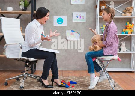 Angry young female psychologist screaming girl sitting with teddy bear Stock Photo