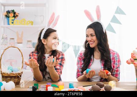 Happy mother daughter holding easter eggs hand looking each other home Stock Photo