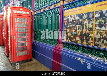 Traditional red London telephone boxes are seen outside the colourful railings of Smithfield Market with a poster showing the faces of market traders Stock Photo