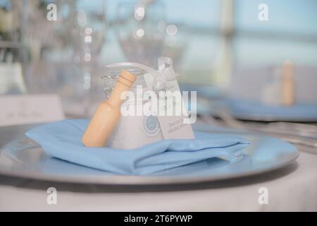 Beautiful Sea Salt filled clear jar with white bow wedding favor with wood on blue blanket on trey in front of white bokeh Stock Photo